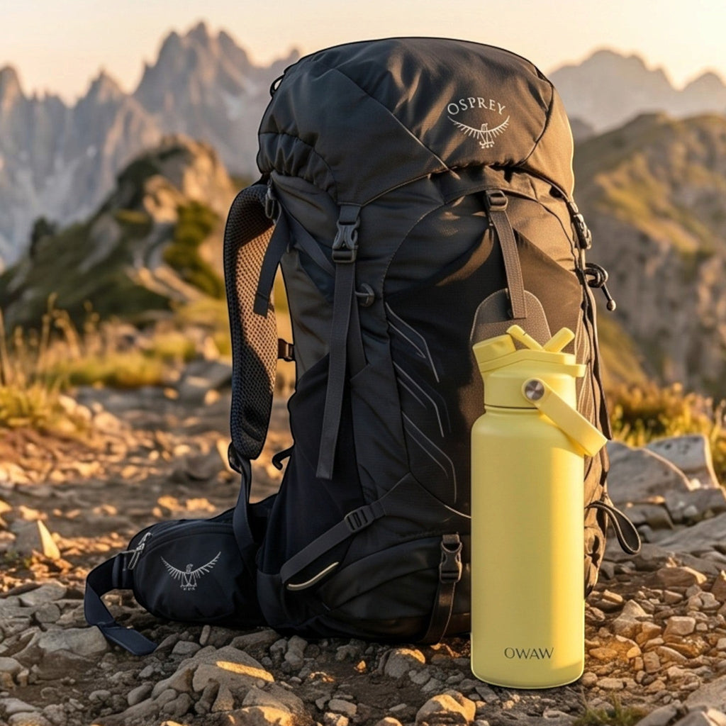 OWAW Nomade stainless steel water bottle in Citrus on a mountain trail beside a hiking backpack
