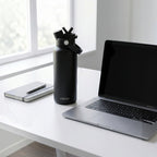 OWAW Nomade stainless steel water bottle in Matte Black on a desk beside a laptop
