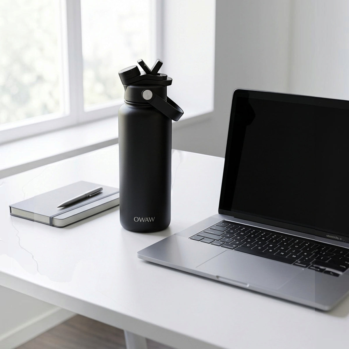 OWAW Nomade stainless steel water bottle in Matte Black on a desk beside a laptop