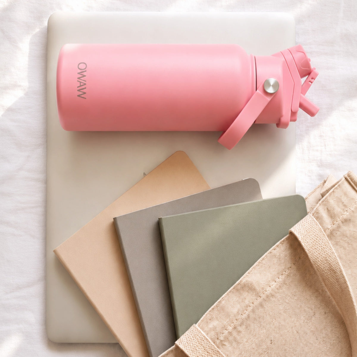 OWAW Nomade stainless steel water bottle in Pink on a laptop with notebooks and a canvas tote